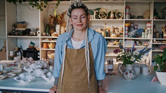 Lady potter stands leaning on worktable in ceramic studio