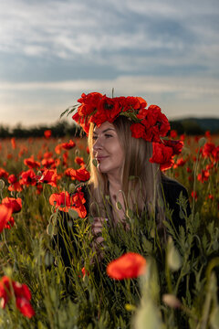 Summer evening portrait of adult woman wearing floral crown in Papaver rhoeas field during sunset