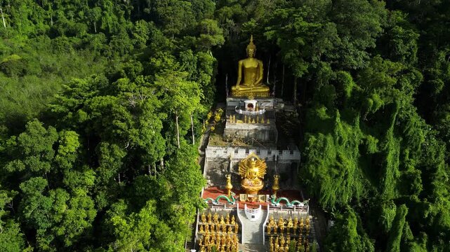 Aerial view of majestic golden Buddha statues nestled within lush tropical rainforest landscape at Wat Tham Sua in Krabi Thailand.