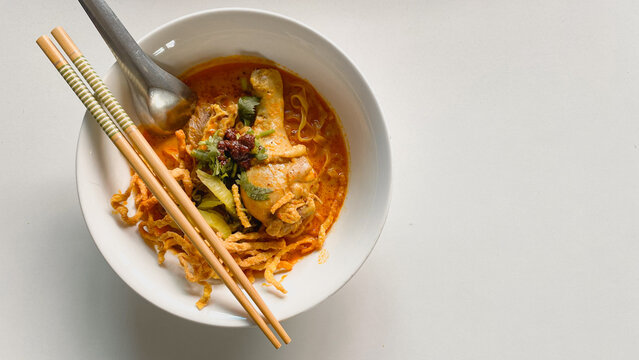 Traditional Northern Thai chicken khao soi curry noodle soup served with tender chicken, crispy noodles, pickled mustard greens, fresh herbs, and rich aromatic coconut curry broth in a white bowl.