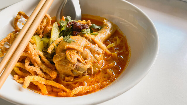 Traditional Northern Thai chicken khao soi curry noodle soup served with tender chicken, crispy noodles, pickled mustard greens, fresh herbs, and rich aromatic coconut curry broth in a white bowl.