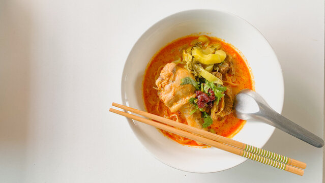 Traditional Northern Thai chicken khao soi curry noodle soup served with tender chicken, crispy noodles, pickled mustard greens, fresh herbs, and rich aromatic coconut curry broth in a white bowl.