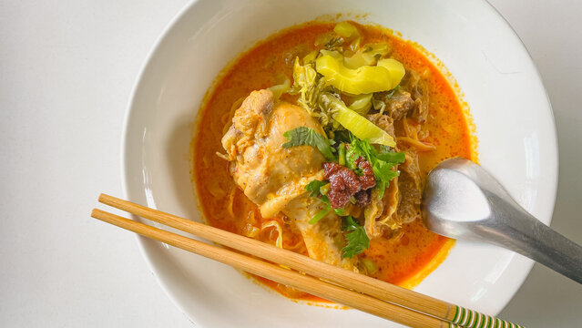 Traditional Northern Thai chicken khao soi curry noodle soup served with tender chicken, crispy noodles, pickled mustard greens, fresh herbs, and rich aromatic coconut curry broth in a white bowl.