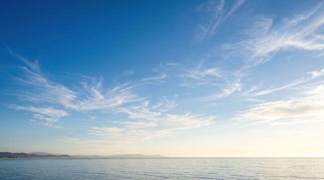 A vast, open ocean with a clear blue sky and scattered white clouds, with a distant landmass visible on the horizon. 