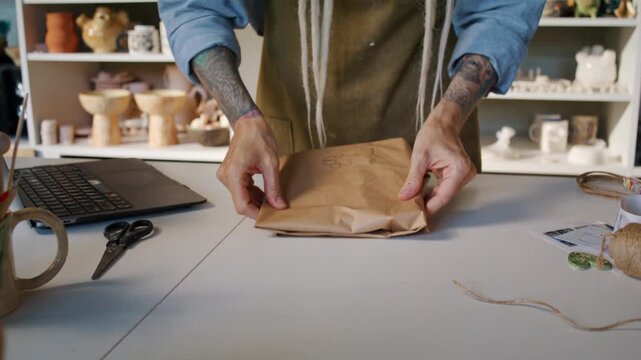 Potter seals wrapped ceramic order with sticker at worktable