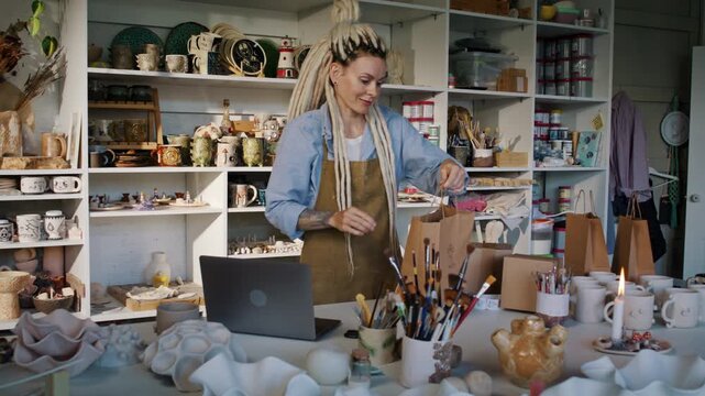 Woman potter places wrapped ceramic order into kraft paper bag