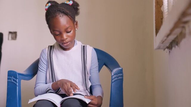 Young black daughter reading in blue plastic chair, braided pigtails with beads, finger tracing words, soft window light, intimate home interior, concentrated expression while studying storybook