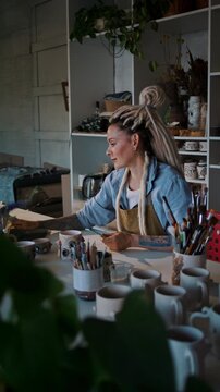 Lady potter measures ceramic mug entering data into store site