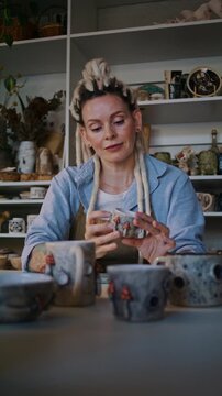 Woman potter inspects handmade ceramic bowl at workshop table