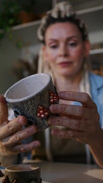 Lady potter examines decorated ceramic bowl before customer sale