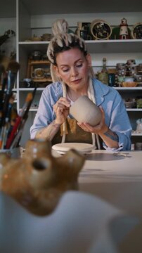 Potter perfects ceramic vessel surface with fine tool in studio