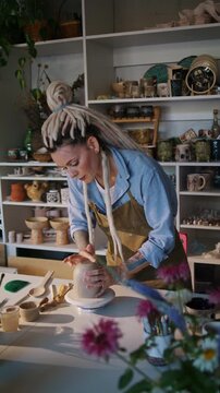Female potter smooths ceramic mug surface with hands in studio