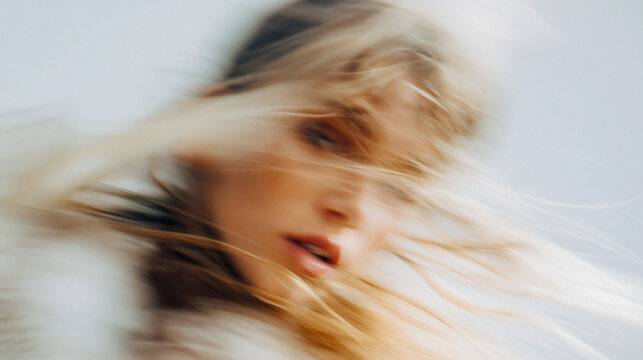 Blonde woman gazes forward while her features shift in soft motion blur creating a minimalist and artistic effect against a neutral background during the bright daylight