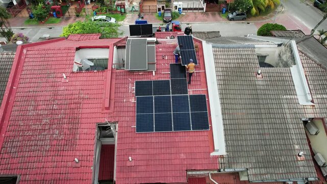 Aerial view of unrecognizable workers installing solar photovoltaic or PV panels onto red rooftop of residential house in Malaysia