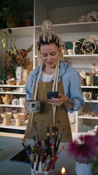 Lady potter checks smartphone while holding decorated ceramic mug