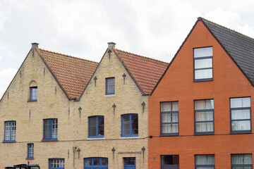 Naklejka premium Historic brick and stone buildings with gabled roofs in a row, featuring blue windows and a mix of red and yellow facades against a cloudy sky