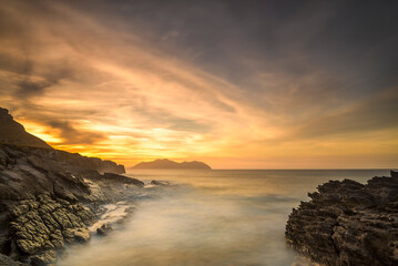 Obraz premium Dramatic sunset sky over rocky coast with long exposure flowing sea waves in Sonabia Cantabria Spain