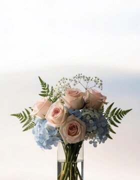 Delicate bouquet of pink roses blue hydrangeas and white baby's breath flowers with ferns in glass vase studio close-up shot.