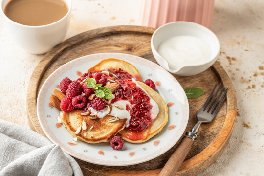 Yummy pancakes with greek yogurt, raspberry jam, fresh berries and mint on wooden tray. Sweet breakfast