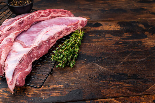 Raw Uncooked lamb ribs breast cut on metal rack with thyme and peppercorns dark wood background butcher style meat with copy space