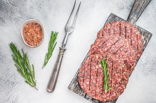 Fresh raw minced beef and lamb burger cutlets with grill pattern rosemary and salt. Overhead view on light stone background with copy space.