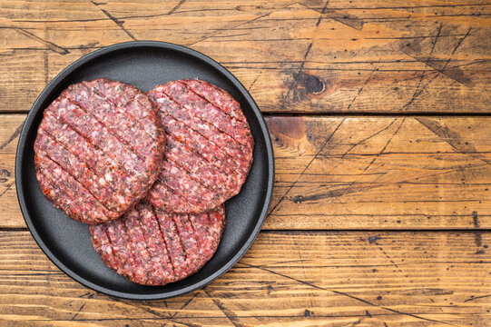 Raw mixed meat patties made from beef and lamb with herbs and spices. Rustic wooden background flat lay with copy space.