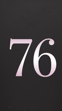 Pink Glitter Blows Away and Reveals the Number 76 on Solid Background