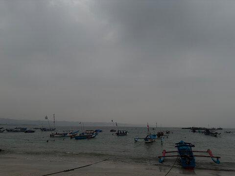 Traditional wooden fishing boats floating on calm ocean water under a heavy overcast gray sky at coastal beach scenery with soft natural daylight captured during a peaceful morning maritime expedition
