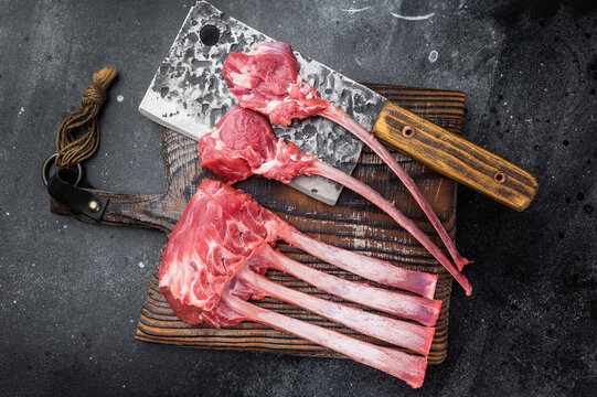 Premium raw lamb rack and sliced cutlets with bone on rustic board dark background culinary butcher style