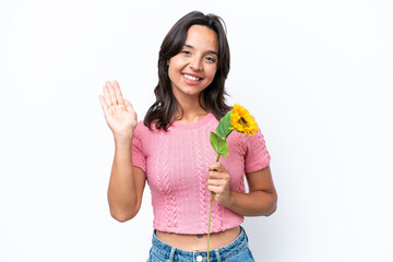 Young hispanic woman holding sunflower isolated on white background saluting with hand with happy expression © luismolinero