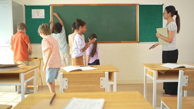Diverse students writing on chalkboard in classroom, representing active learning