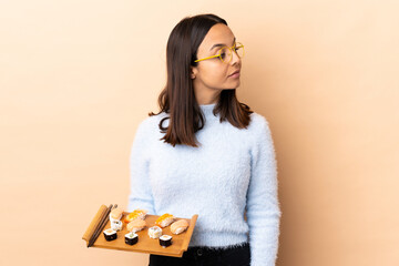 Young brunette mixed race woman holding sushi over isolated background . Portrait © luismolinero