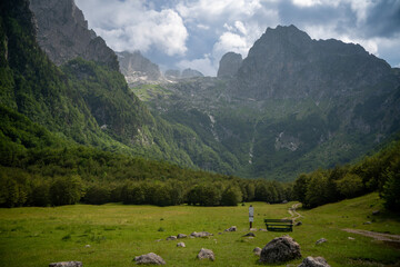 Obraz premium Wooden bench in a green meadow with a majestic view of mountain peaks in Grebaje valley, Montenegro.