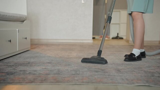 White woman vacuuming house rug closeup showing feet and nozzle on textured fibers, deliberate strokes along edge, canister hose in background, rhythmic satisfying motion, focused cleaning detail