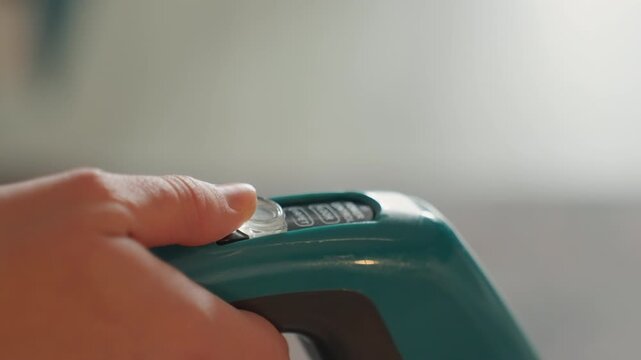 White woman pressing vacuum handle button, tight macro of finger engaging power switch, ergonomic grip, teal plastic body, soft background blur, modern cordless stick in active house cleaning