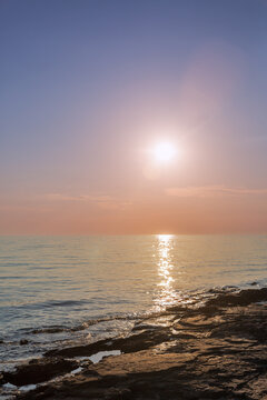 Sunset over calm sea and rocky shore.