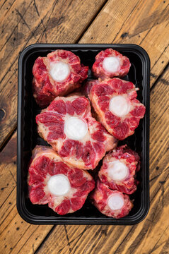 Fresh uncooked mutton lamb oxtail cuts with marrow bones packaged in tray, overhead composition on wooden background