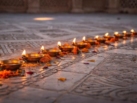 Brass Diya Lamps and Loose Marigold Petals on Ornate Stone Courtyard at Dusk｜石造りの中庭に並ぶ真鍮のディヤランプとマリーゴールドの花びら