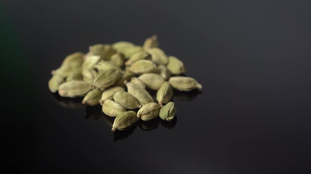 A close-up shot of green cardamom pods, Elettaria cardamomum, slowly rotate against a black background, highlighting the aromatic spice's texture and color