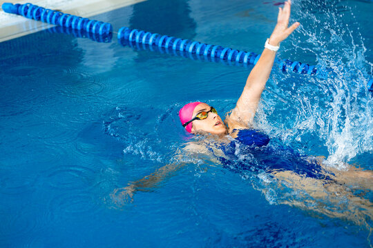 Female athlete performing backstroke in a swimming pool, focusing on health and improvement