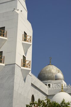 white marble mosque minaret tower and main dome with golden crescent against blue sky