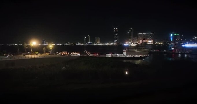Phnom Penh night skyline with vehicles disembarking from a ferry that has just arrived at the riverbank.