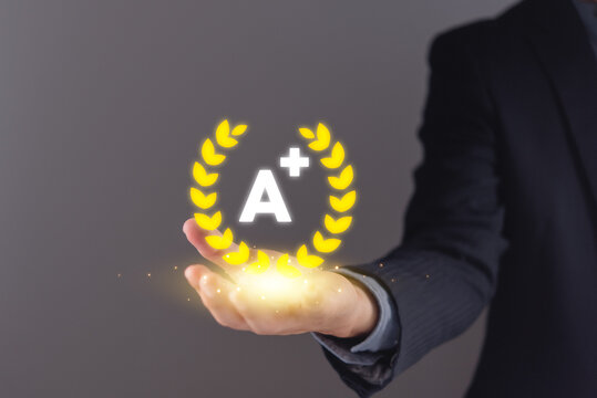 Businessman hand holding glowing yellow A plus laurel wreath hologram for excellence concept