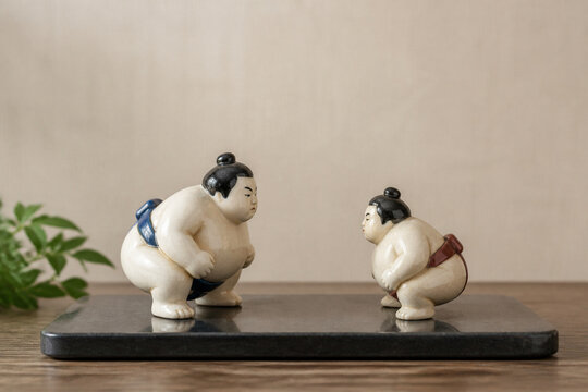 Two ceramic sumo wrestler figurines on dark stone tray, balance and friendly rivalry concept
