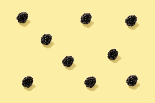 Scattered blackberries on a pale yellow background, shown from above in a simple minimal flat lay with copy space.