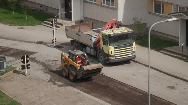 Skid steer loader excavating and loading debris onto dump truck in Estonia road construction
