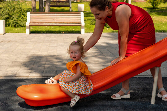 Mother Helps Toddler Daughter Finish Playground Slide