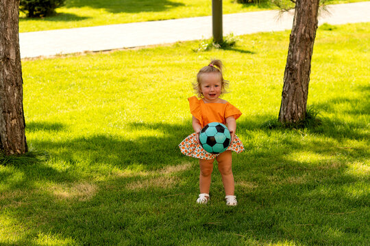 Happy Toddler Girl Holding Soccer Ball on Green Lawn