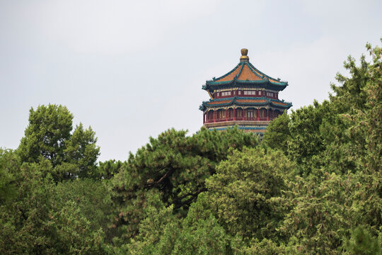 Traditional Chinese pavilion rising above lush green trees at the Summer Palace in Beijing, China. The ornate multi-tiered architecture features distinctive Chinese rooflines