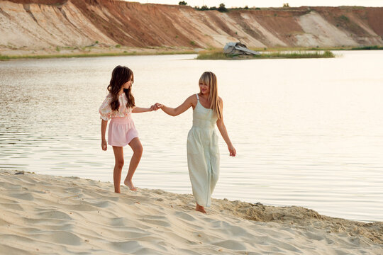 Mother And Young Daughter Holding Hands On Sandy Shore